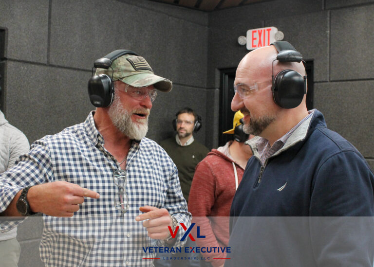 Two men engage in conversation inside an armory. Both men are wearing eye and ear protection.