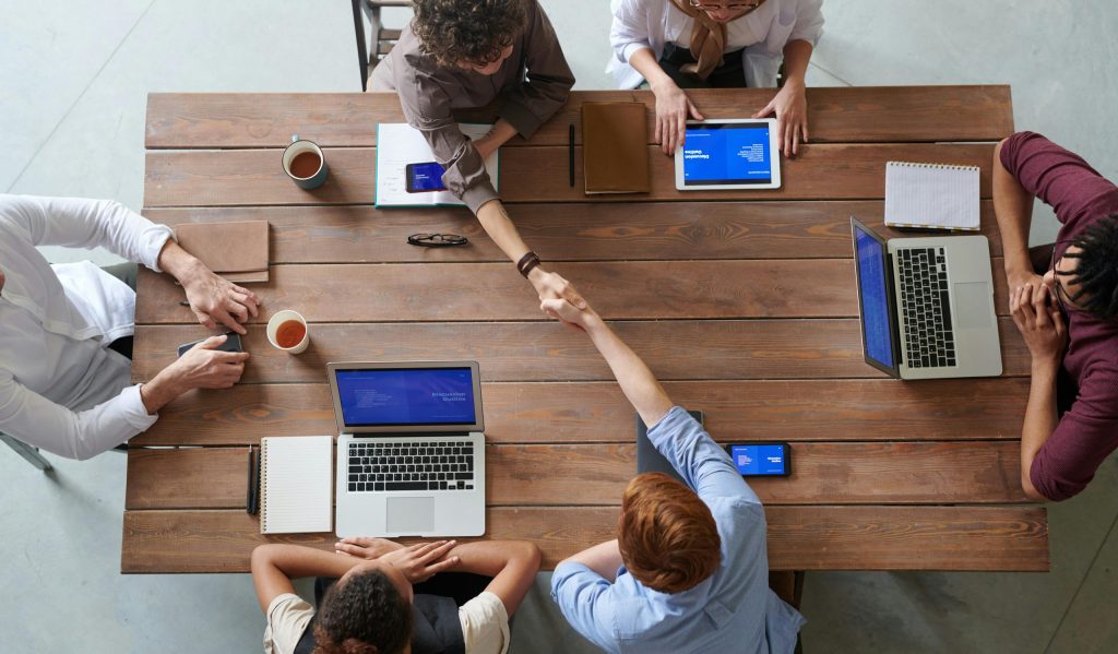 Overhead view of colleagues in a work meeting using laptops and tablets, emphasizing teamwork and technology.